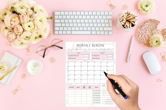 Close-up of a woman's hand filling out the monthly book tracking section of a printable reading journal.