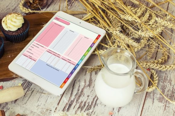 A hyperlinked monthly digital planner on a table with a cup of milk.